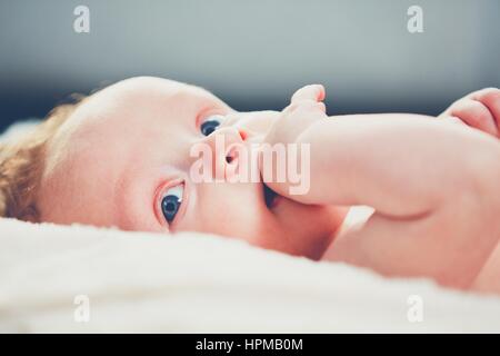 Kleines Baby mit blauen Augen und Hand in den Mund. Stockfoto