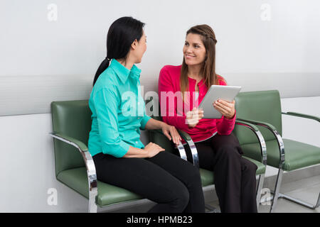 Lächeln der Patientin mit digital-Tablette während im Gespräch mit Frau am Krankenhaus lobby Stockfoto