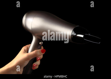 Haartrockner in weiblicher Hand. Schwarzer Hintergrund. Hand mit rot lackierten Nägeln Stockfoto