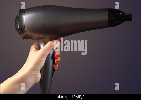 Haartrockner in Frau hand auf farbigem Hintergrund. Hand mit roten Nägeln. Stockfoto