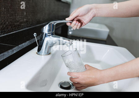 Füllen ein Glas Wasser aus Edelstahl oder Chrom Wasserhahn oder Wasserhahn, Frau hautnah auf ihre Hand und das Glas mit fließendem Wasser und Luftblasen. Stockfoto