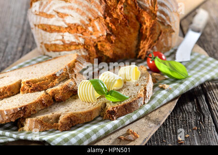 Frisch gebackenes Brot mit Butter-Brötchen serviert auf einem alten Holzbrett Backen Steinofen Stockfoto