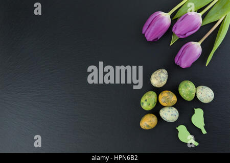 Bunte Wachteleier und Tulpe Blumen und grünen hölzernen Vögel am Steintisch. Draufsicht mit Textfreiraum. Studioaufnahme. Stockfoto