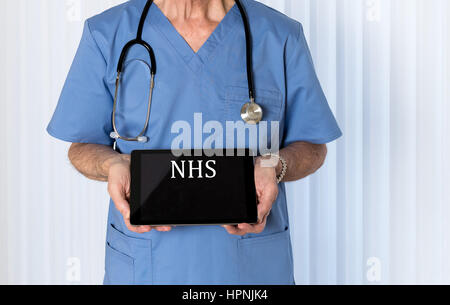 Senior männlicher kaukasischer Arzt mit Stethoskop in medizinischen Peelings nachschlagen und halten elektronische Tablet für NHS-Nachricht Stockfoto