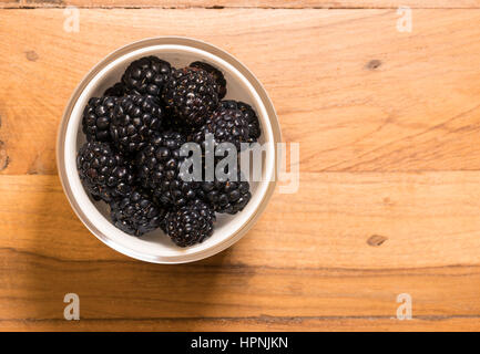 Antenne oder Top Blick auf eine weiße Glasschale von Bio Brombeeren frisch gewaschen und sitzen auf dem alten Holztisch Oberfläche Stockfoto