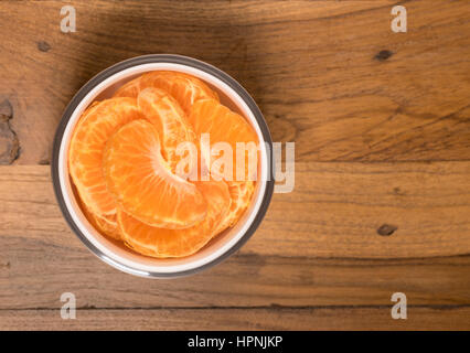 Antenne oder Top Blick auf eine weiße Glasschale von Bio Orange oder Mandarine Scheiben frisch gewaschene und sitzt auf alten Holztisch Oberfläche Stockfoto