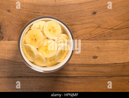 Antenne oder Top Blick auf eine weiße Glasschale von organischen Bananenscheiben frisch gewaschen und sitzen auf dem alten Holztisch Oberfläche Stockfoto