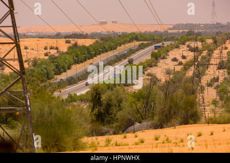 AL AIN, Vereinigte Arabische Emirate - Autobahn durch Wüste mit bewässerten Bäumen und Sträuchern am Rand. Stockfoto