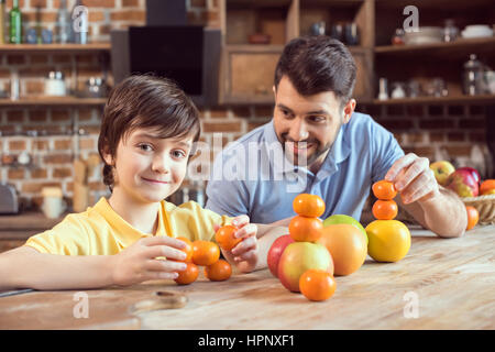 Vater und Sohn spielen mit Zitrusfrüchten am Küchentisch Stockfoto