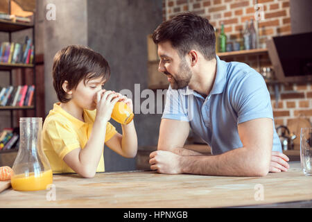 Vater, Blick auf die niedlichen kleinen Sohn frischen gepressten Orangensaft trinken Stockfoto