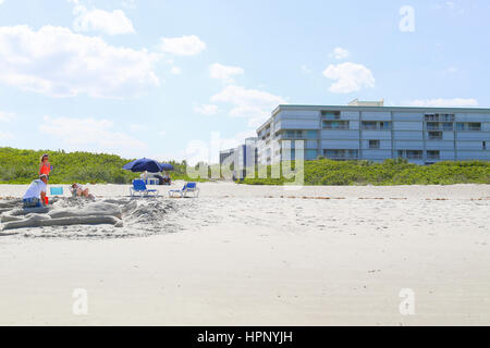 Cocoa Beach, USA - 7. Mai 2015: Familie am Strand bauen eine Sandburg mit einem Strand Stuhl Vermietung und Hotels in den Rücken. Stockfoto