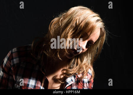 Porträt einer jungen Frau mit langen, blonden Haaren, die Spaß am Fotografieren mit verschiedenen Kleidern hat, Studio-Aufnahme mit schwarzem Hintergrund Stockfoto