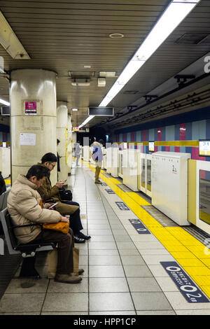 Pendler, die mit ihren Handys während des Wartens auf den nächsten Zug an der Edogawabashi Station, Tokio, Japan. Stockfoto