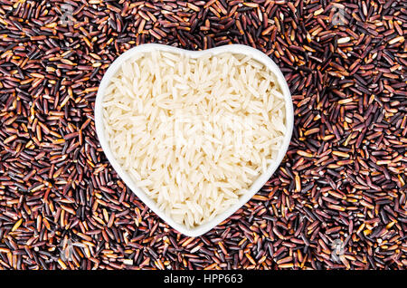Roher Reis in Herz-Form-Schüssel auf Reis Beere Hintergrund. Stockfoto