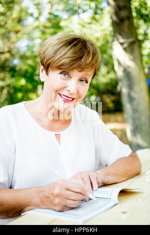 Porträt von lächelnden senior Frau tun einen Kreuzworträtsel im freien Stockfoto