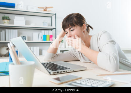 Verträumte junge Geschäftsfrau sitzen am Schreibtisch, mit einem Laptop arbeiten und Gähnen Stockfoto