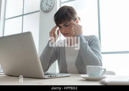 Erschöpfte junge Frau, die Arbeiten am Schreibtisch berühren ihre Tempel, sie hat eine starke Kopfschmerzen, stressigen Leben und Krankheit-Konzept Stockfoto