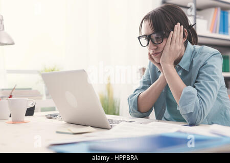 Gelangweilte junge Frau im Büro mit einem Laptop arbeiten und starrte auf Bildschirm Stockfoto