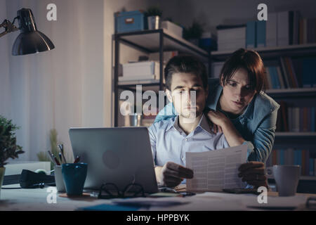 Junges Paar mit einem Computer, Überprüfung von Rechnungen und Papierkram spät in der Nacht sind sie besorgt und traurig Stockfoto