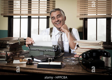 Lächelnde Reporter arbeiten am Schreibtisch mit Vintage Schreibmaschine, 1950er-Jahre Stil. Stockfoto