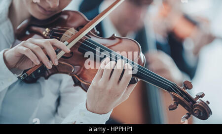 Talentierte Geigerin ihr Geigenspiel mit Klassik Orchester auf Hintergrund Stockfoto