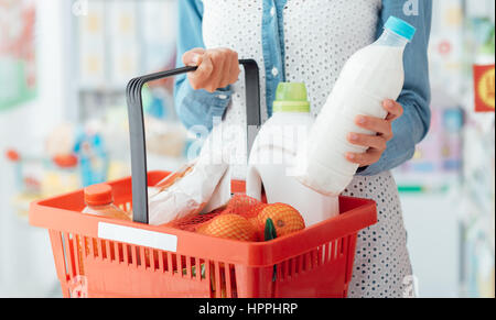 Frau einkaufen im Supermarkt, sie tragen einen Warenkorb und nehmen eine Milchflasche Stockfoto