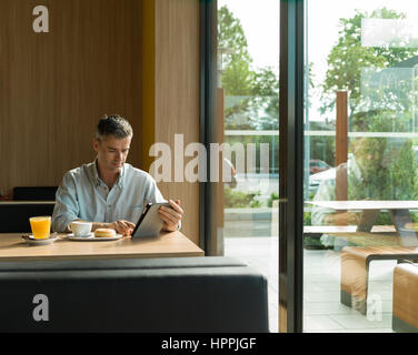 Geschäftsmann mit einem gesunden entspannten Frühstück an der Bar, er ist mit einer digital Touch-Screen-Tablette und sitzt neben einem Fenster Stockfoto