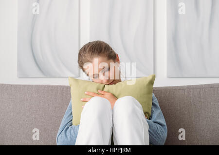 Traurig depressiven Frau zu Hause, ist sie sitzen auf der Couch und umarmt eine Kissen, Einsamkeit und Traurigkeit Konzept Stockfoto