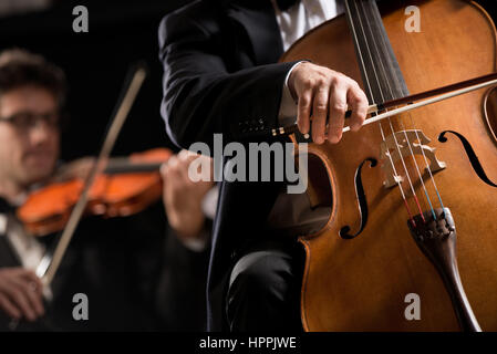 Professionelle Cellisten mit Symphony Orchestra Konzert auf Hintergrund. Stockfoto