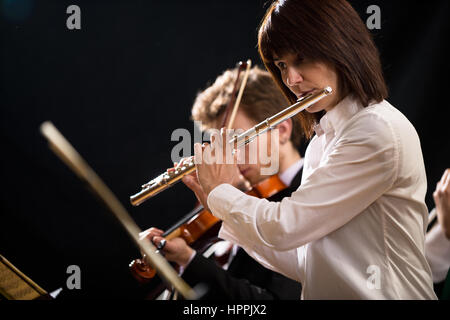 Elegante weibliche Flötist auf der Bühne mit Orchester. Stockfoto