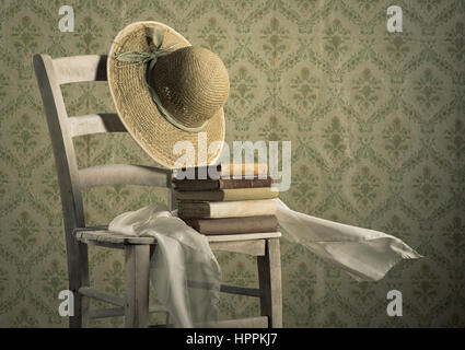 Stapel von antiken Büchern auf einem Stuhl mit Strohhut und Kopftuch, Vintage Wallpaper auf Hintergrund. Stockfoto