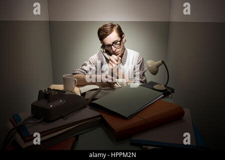 Retro-Geek am Telefon mit unordentlichen Schreibtisch in einem kleinen Raum. Stockfoto