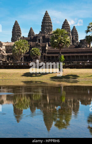 Eine klassische Ansicht von Angkor Wat spiegelt sich im Wasser vor dem Haupteingang an einem sonnigen Tag mit blauem Himmel. Stockfoto