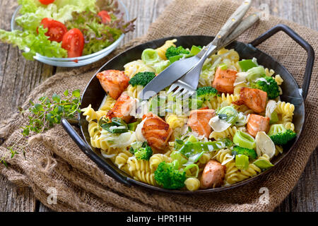 Italienische Pasta mit gebratenem Lachsfilet, Meerrettich und einer Sauce aus Sahne und Lauch in einer eisernen Pfanne mit einem Beilagensalat serviert Stockfoto