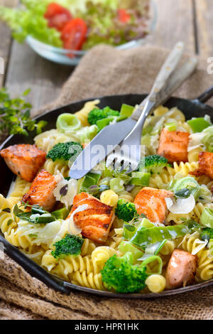 Italienische Pasta mit gebratenem Lachsfilet, Meerrettich und einer Sauce aus Sahne und Lauch in einer eisernen Pfanne mit einem Beilagensalat serviert Stockfoto