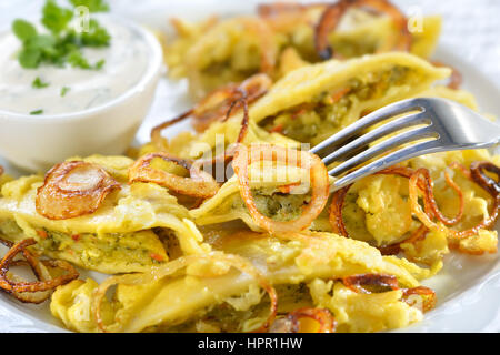 Fried schwäbischen Ravioli (so-called'Maultaschen ") mit vegetarischer Füllung serviert mit gerösteten Zwiebeln, Rührei, Ei und cremige Kräuterkäse Stockfoto