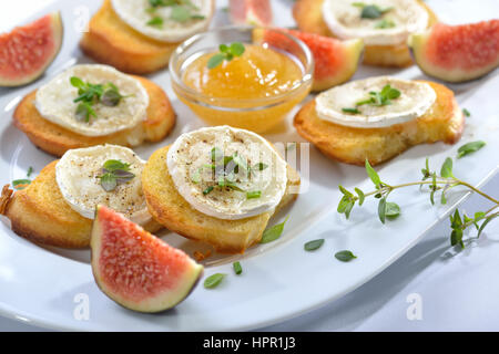 Gebackene Vorspeisen pikante Crostini mit Ziegenkäse und frischen Kräutern, serviert auf einem weißen Teller mit Feigensenf und frischen Feigen Stockfoto