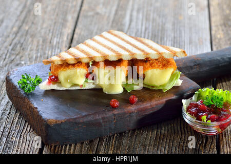 Getoastete Panini Dreiecke mit panierte Mini-Camembert Käse Brote, Cranberries und Eisbergsalat, serviert auf einem Holzbrett Stockfoto