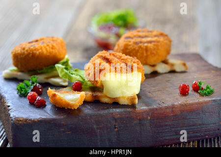 Getoastete Panini Dreiecke mit panierte Mini-Camembert Käse Brote, Cranberries und Eisbergsalat, serviert auf einem Holzbrett Stockfoto