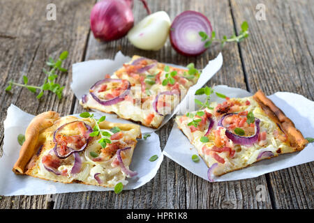 Suppen: Scheiben heiße gebackene Flammkuchen Flammkuchen aus dem Elsass mit Zwiebeln, Speck und Sauerrahm serviert auf Butterbrotpapier Stockfoto