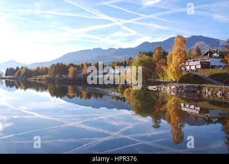 Reflexionen der Flugzeuge Kondensstreifen Criss cross den blauen Himmel über dem Etang Long und der Golfplatz in Crans Montana, Schweiz Stockfoto