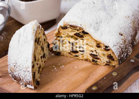 Hausgemachte Christstollen Stück auf Holzbrett mit Messer, Zutaten im Hintergrund, Ansicht von oben abschneiden, Nahaufnahme Stockfoto