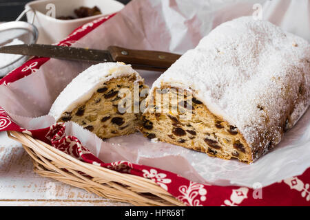 Hausgemachter Christstollen mit abgeschnittenen Stück mit Messer im Weidenkorb, Küchentuch, Zutaten, Ansicht von oben Stockfoto