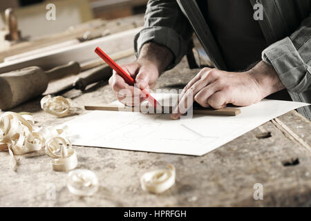 Detailansicht eines Tischlers, die mit einem roten Stift zum Zeichnen einer Linie auf eine Blaupause Stockfoto