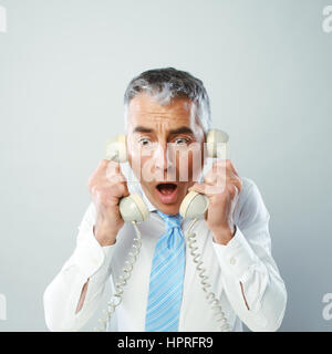 Ein gestresster Geschäftsmann sprechen in zwei Mobilteile, die er in der Hand. Stockfoto
