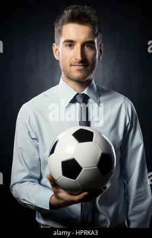 Junge attraktive Geschäftsmann hält einen Fußball und lächelnd. Stockfoto