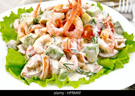 Salat mit Garnelen, Avocado, Tomaten und Mayonnaise auf den Salat auf dem Teller, Serviette, Gabel auf dem Hintergrund Licht Holzbrett Stockfoto