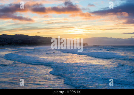 Dunedin, Otago, Neuseeland. Einsamer Surfer trotzen die stürmischen Gewässern des Pazifischen Ozeans vor St Clair Beach, Sonnenaufgang. Stockfoto