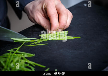 Küchenchef, schneiden grüne Erbse auf die schwarze Schneidebrett Stockfoto