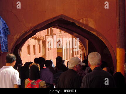 Massen von Touristen unter Bogen des alten Dorfes Abyāneh und roten Fassaden der Adobe-Häuser und Märkte Stockfoto